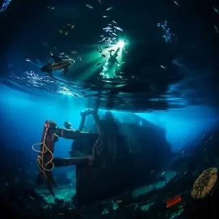 A dramatic underwater scene of a shipwreck surrounded by marine life, with beams of light illuminating the eerie beauty of the sunken vessel.