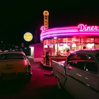 A retro vintage photograph of a 1950s diner, complete with classic cars parked outside, neon signs glowing warmly, and people enjoying milkshakes at the counter.